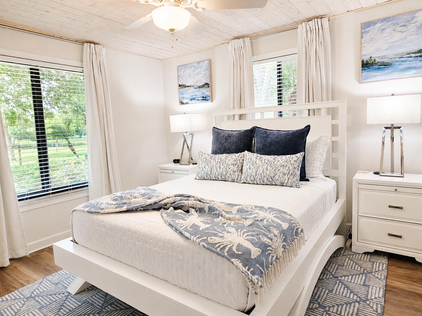Bright bedroom with white furnishings, blue pillows and coastal artwork